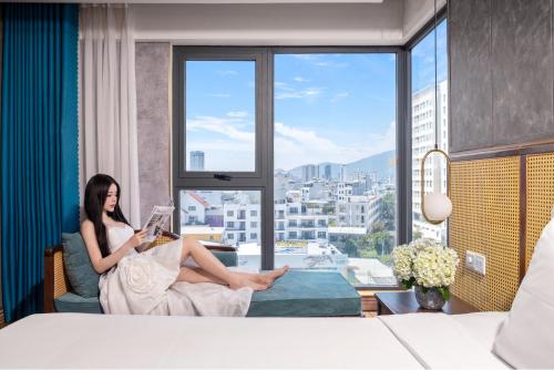 a woman sitting on a couch reading a book in front of a window at White Sand Boutique Hotel in Danang