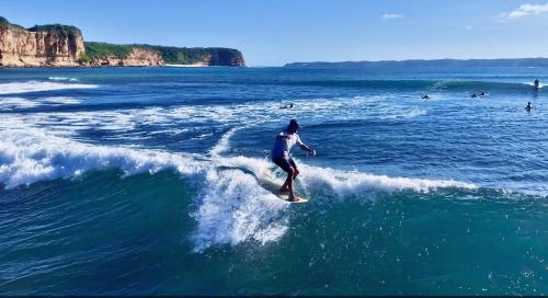 a man riding a wave on a surfboard in the ocean at Ombak Resort at Ekas , a luxury surf and kite destination, Close to Inside Ekas beach in Ekas