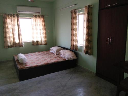 a bedroom with a bed with two pillows and two windows at Nalanda Tulip in Kolkata
