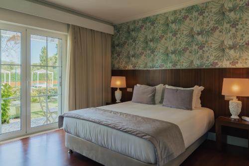 a bedroom with a bed and a large window at Quinta do Pinheiro Hotel E Eventos by Grupo Quinta dos Lagos in Valado dos Frades
