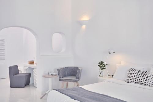 um quarto branco com uma cama e uma cadeira em Cliff Side Suites em Firostefani