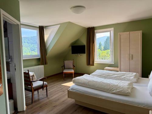 a bedroom with a bed and two chairs and two windows at Hotel Markgräfler Hof in Badenweiler