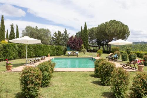 a swimming pool in a yard with umbrellas at Villa Campriano by VacaVilla in Pienza