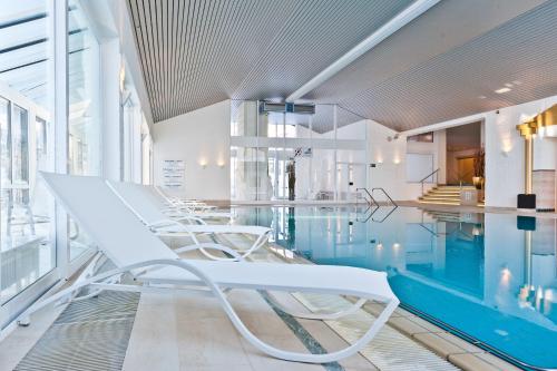 - une piscine avec des chaises blanches dans un bâtiment dans l'établissement MONDI Resort und Chalet Oberstaufen, à Oberstaufen
