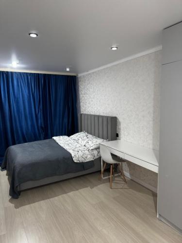 a bedroom with a bed and a desk and a blue curtain at Квартира 2 комнаты in Balqash