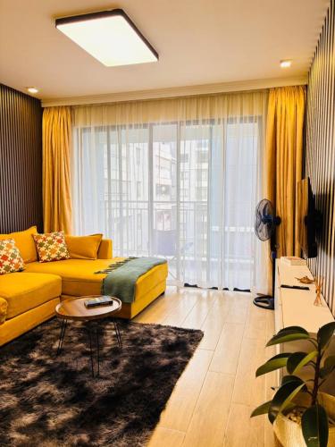 a living room with a yellow couch and a large window at Two-Bedroom Apartment Near JKIA & SGR Free Parking & Wi-Fi By Irene in Nairobi