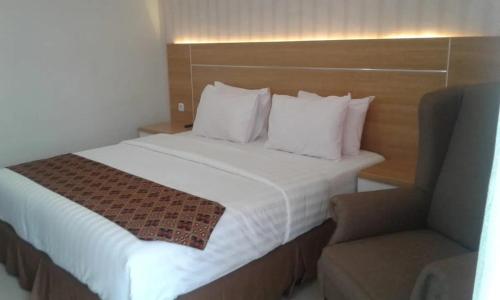 a hotel room with a bed with white sheets and a chair at Hotel Ella Tambolaka in Tambolaka Airport