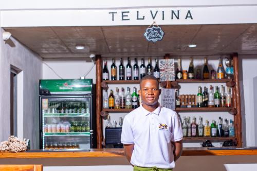 a man standing in front of a bar with alcohol at Telvina Beach Lodge in Vilanculos