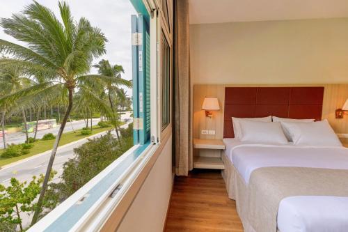 a bedroom with a bed and a window with a palm tree at Viona Beach Hotel - Marina Phu Quoc in Phú Quốc