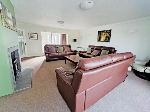 a living room with a leather couch and a fireplace at Tall Pines in Carrbridge
