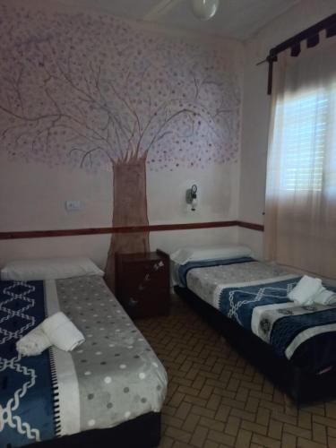a bedroom with two beds and a tree mural on the wall at Hotel Praise in Capilla del Monte