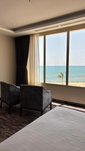 a bedroom with a bed and two chairs and the ocean at Beach Inn in Al Qunfudhah