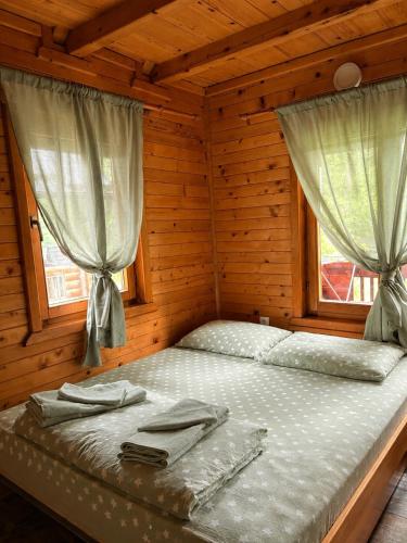 a bed in a wooden room with two windows at Drinka in Ljubovija