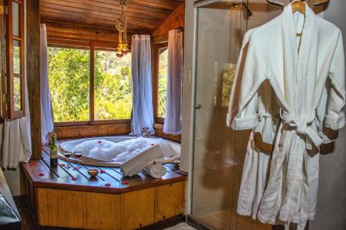 a bathroom with a tub and a window and a robe at Pousada Infinito in Visconde De Maua