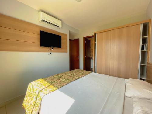 a bedroom with a white bed with a tv on the wall at Apartamento Veredas Flat - Rio Quente in Rio Quente