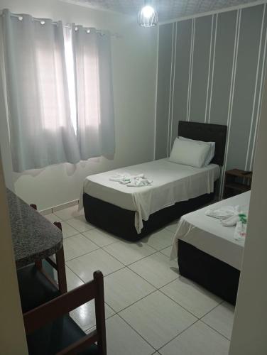 a small room with two beds and a chair at Hotel Maciel in Ponta Grossa