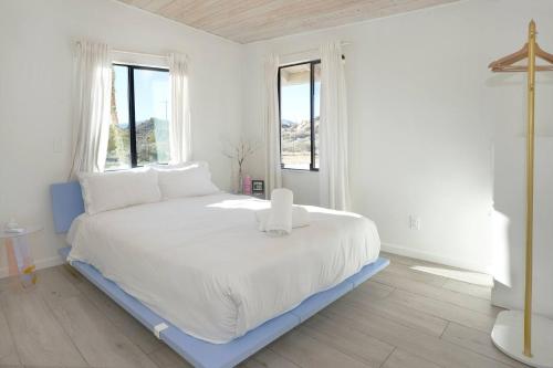a large white bed in a white room with windows at The Giddyup in Pioneertown