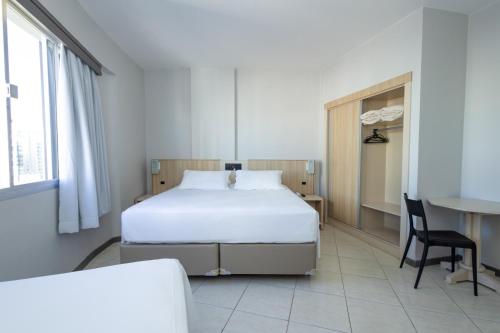 a bedroom with a bed and a desk and a table at Hotel Ilha da Madeira in Balneário Camboriú