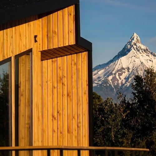 a building with a snow covered mountain in the background at Volcano Suites in Puyehue