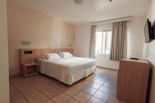 ein Schlafzimmer mit einem weißen Bett und einem Fenster in der Unterkunft Hotel Açores in Balneário Camboriú