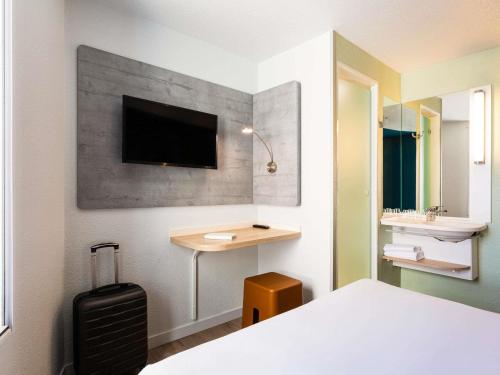 a bedroom with a bed and a desk with a tv on the wall at ibis budget Bordeaux Centre - Gare Saint Jean in Bordeaux