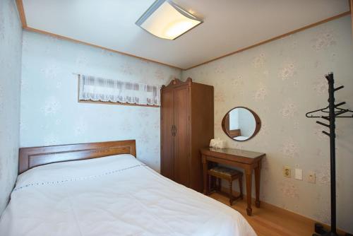 a bedroom with a bed and a mirror and a table at Four Season Pension in Seogwipo