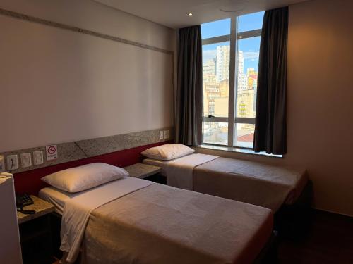 a hotel room with two beds and a window at Center Verdes Pássaros Loft in Porto Alegre