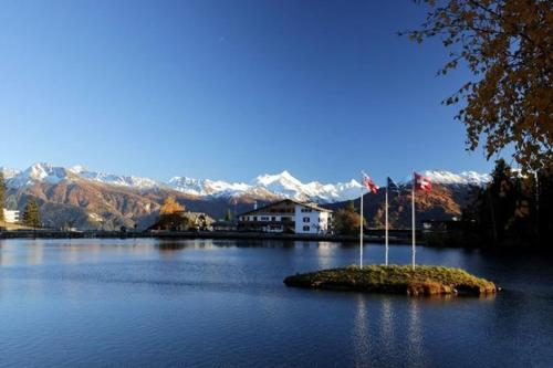 a small island in the middle of a lake with mountains at Hotel du Lac in Crans-Montana