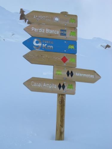 a wooden sign with several signs in the snow at Apartamentos Ball Benas Edificio Prados de Velarta in Cerler