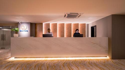 Zwei Personen sitzen an einem Empfangstresen in einem Büro. in der Unterkunft Bond Hotel Rawang in Rawang