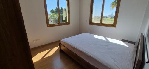 a white bedroom with two windows and a bed at Nautical Nest in Livadhia
