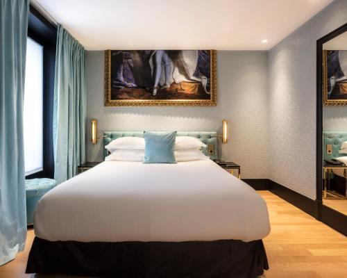 a bedroom with a large white bed with a painting on the wall at Eiffel Petit Louvre in Paris