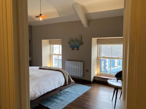 a bedroom with a bed and a desk and two windows at The Loft at Design Bank in Milltown Malbay
