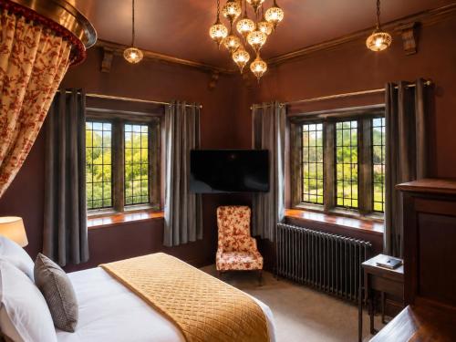 a bedroom with a bed and a chair and windows at Lewtrenchard Manor in Lewdown