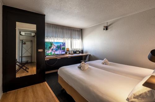 a hotel room with two beds and a television at Hôtel Le Cyrano Bergerac in Bergerac