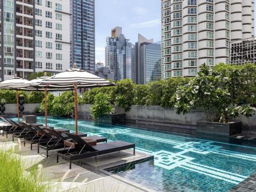 a swimming pool with chairs and umbrellas on a building at Mövenpick Hotel Sukhumvit 15 Bangkok in Bangkok