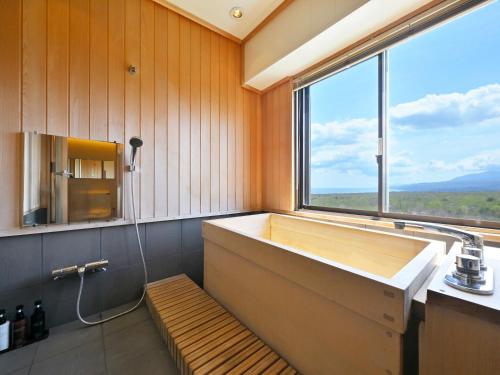 a bathroom with a large tub with a large window at Livemax Resort Hakodate Shikabe Onsen in Shikabe