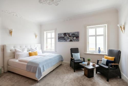 a white bedroom with a bed and two chairs at Kapitänsapartment in der VILLA KAETHE am Kurpark - moderne & stilvolle 65qm Ferienwohnung nahe Strand in Warnemünde
