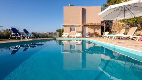 a swimming pool with chairs and an umbrella next to a house at Villa Rubin in Almyrida