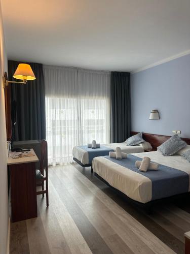 a hotel room with two beds and a table and a desk at Hotel Acacias Suites & Spa in Lloret de Mar