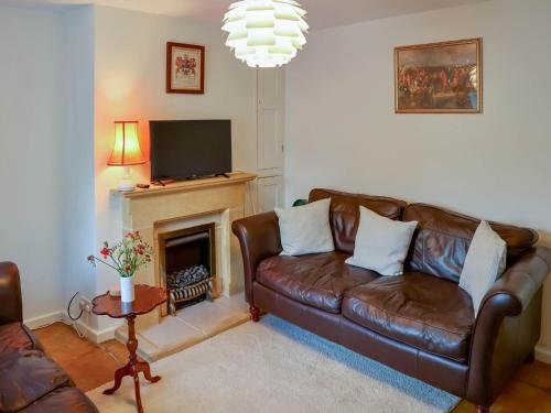 a living room with a brown leather couch and a fireplace at Pam's Cottage in Cheltenham
