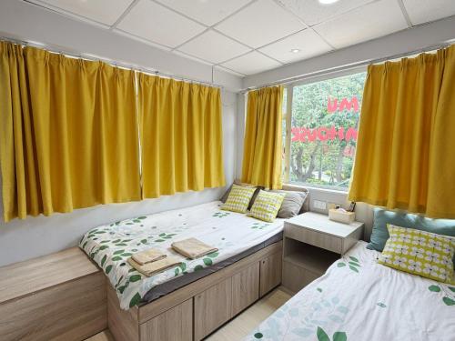 a bedroom with two beds and a window with yellow curtains at AMU Dreamhouse 阿木旅舍 in Hong Kong
