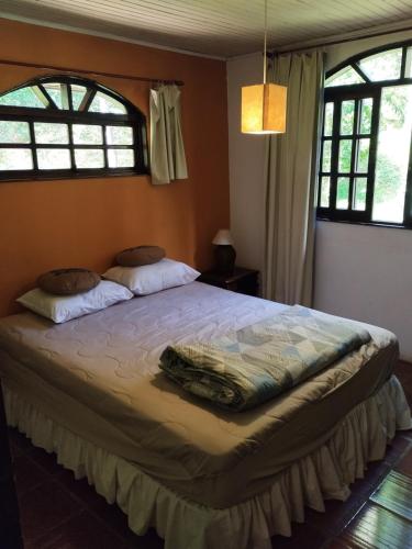 a bedroom with a large bed with two windows at Chácara Luz do Vale in Votuverava