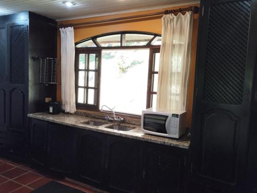 a kitchen with a microwave on a counter with a window at Chácara Luz do Vale in Votuverava