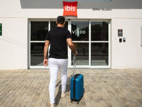 a man pulling a blue suitcase in front of a store at Ibis Serra Talhada in Serra Talhada
