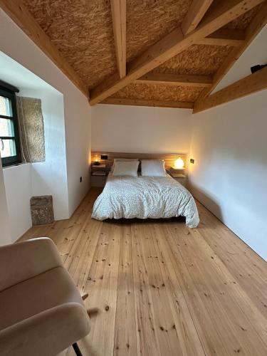 a bedroom with a bed and a chair and wooden floors at PASENIÑO - Aloxamento rural in Palas de Rei