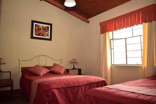 a bedroom with two beds with red sheets and a window at Los Portales de Yungar Ecolodge Huaraz in Carhuaz