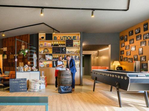 two people standing at a counter in a store with a pool table at Mercure Reims Parc Des Expositions in Reims