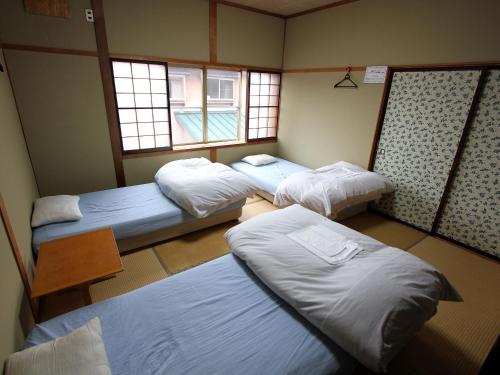 a room with three beds and a table and windows at Towadako Backpackers in Towada