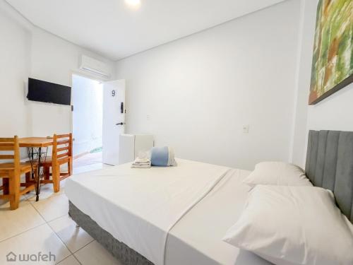 a white bedroom with a bed and a dining room at Wafeh Fleming Suítes Pampulha in Belo Horizonte